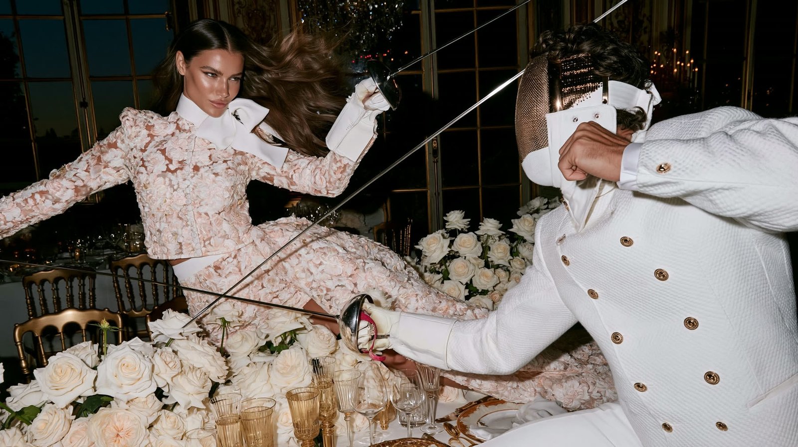 A bride and groom fencing in white couture among white roses