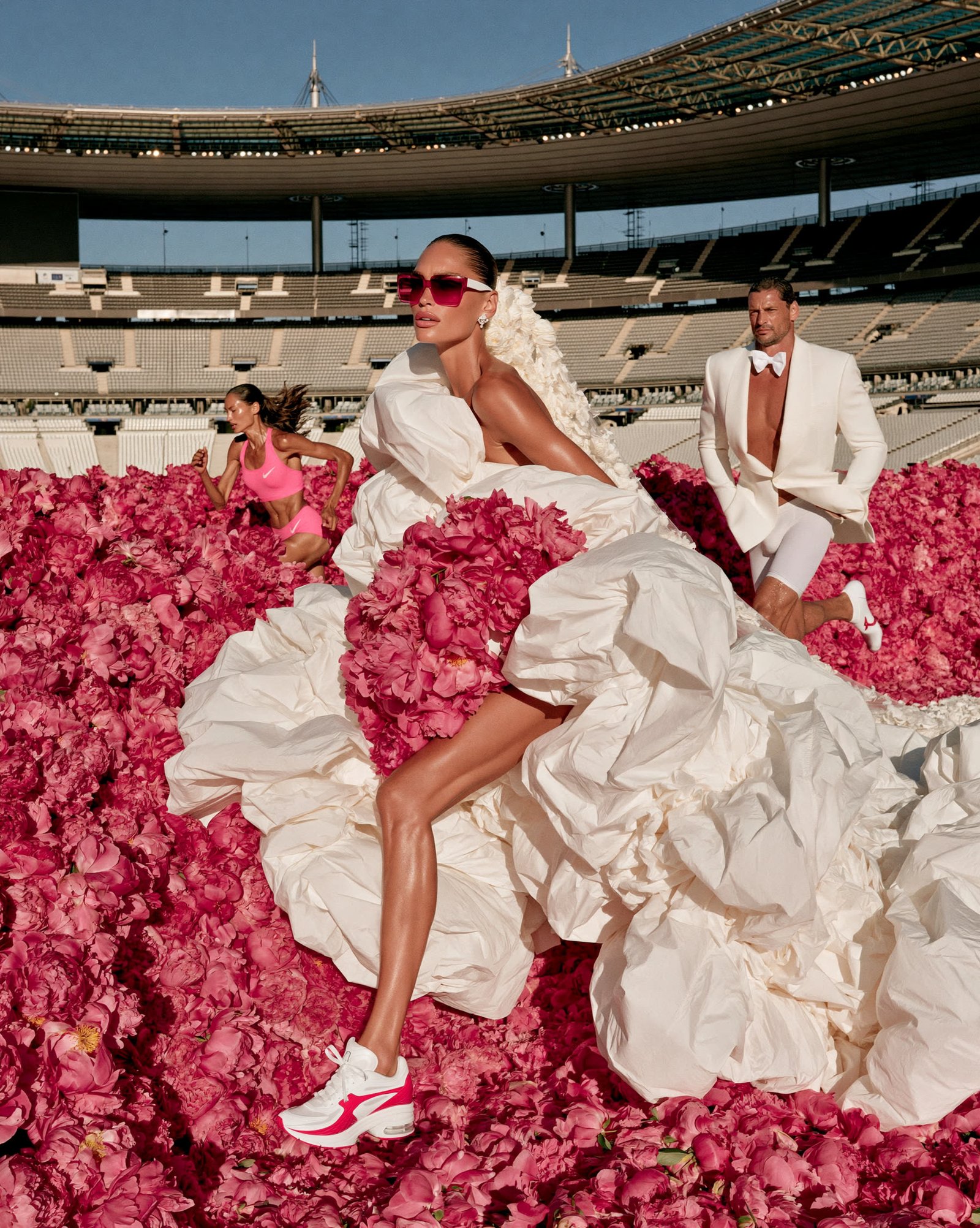Bride in a cream ruffled gown reclining on a bed of rose petals in an Olympic stadium
