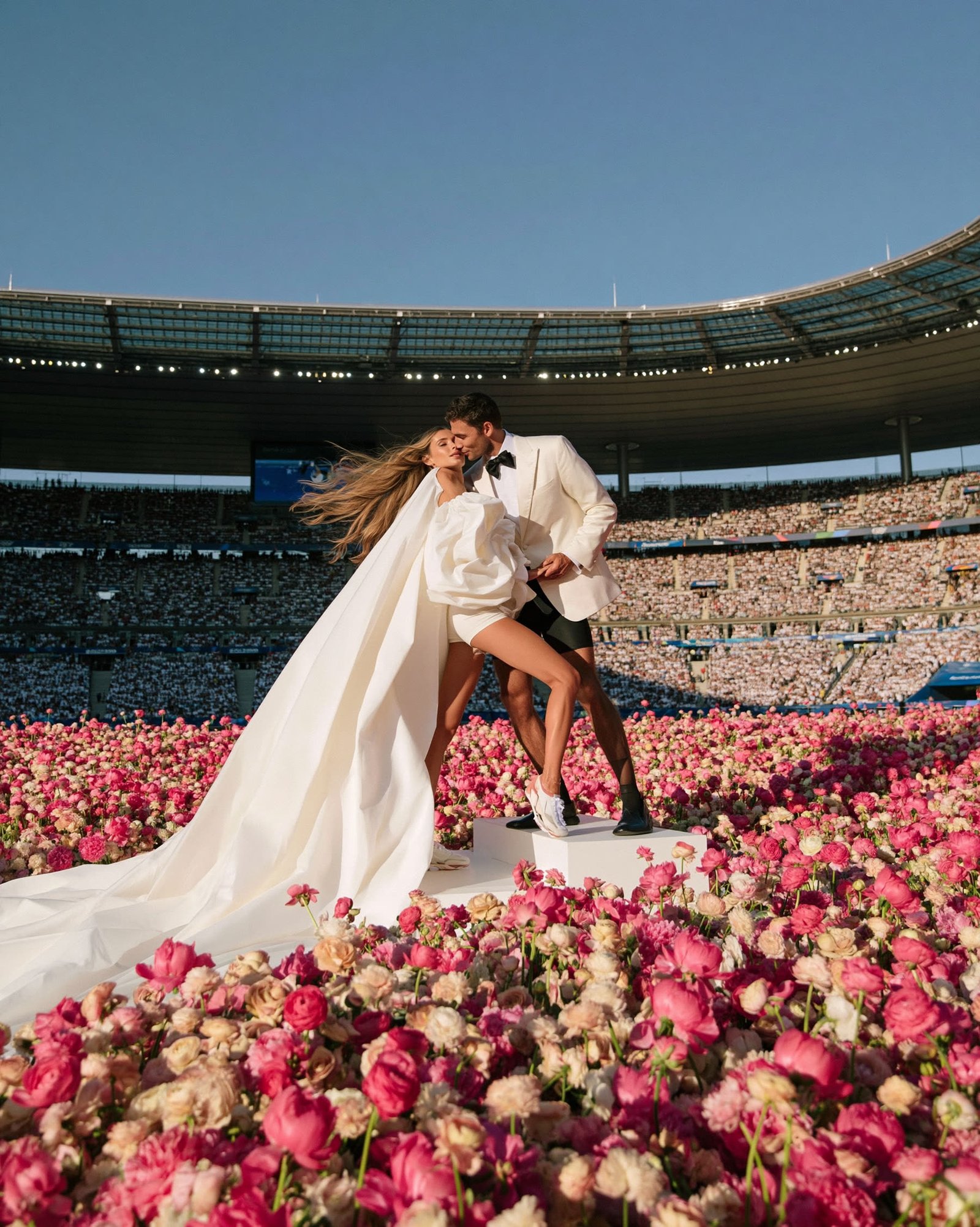 Bride in a flowing gown sprinting across a stadium field carpeted in rose petals