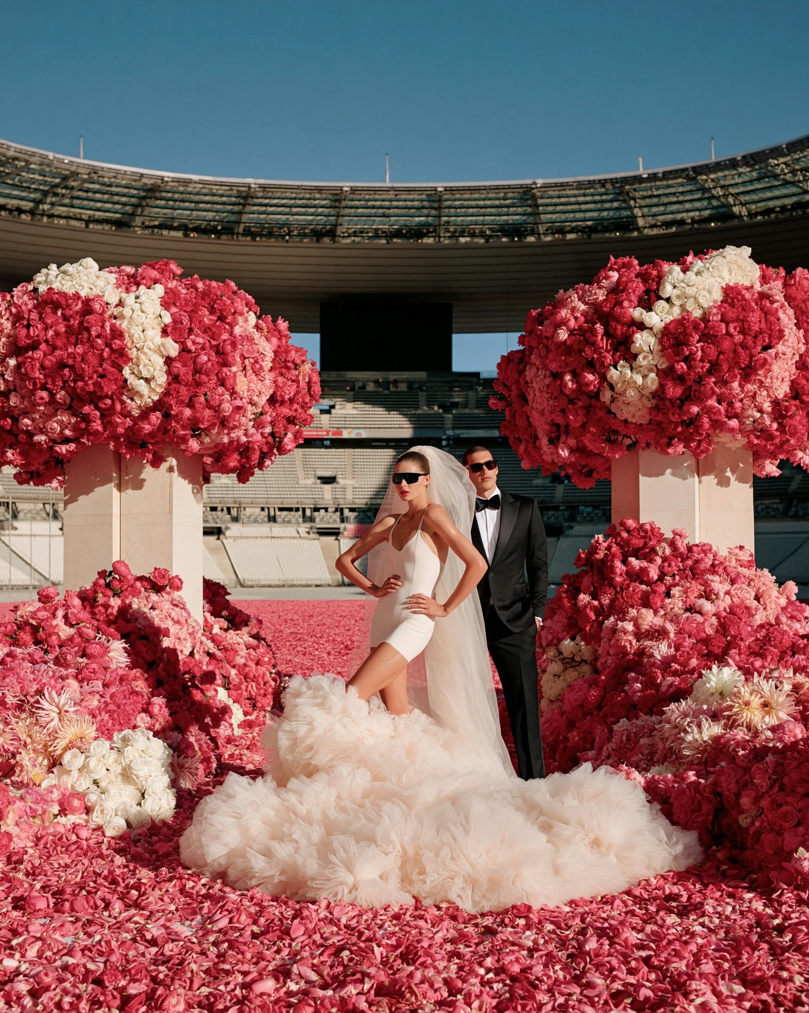 A bride and groom among towering floral installations in a petal-filled Olympic stadium