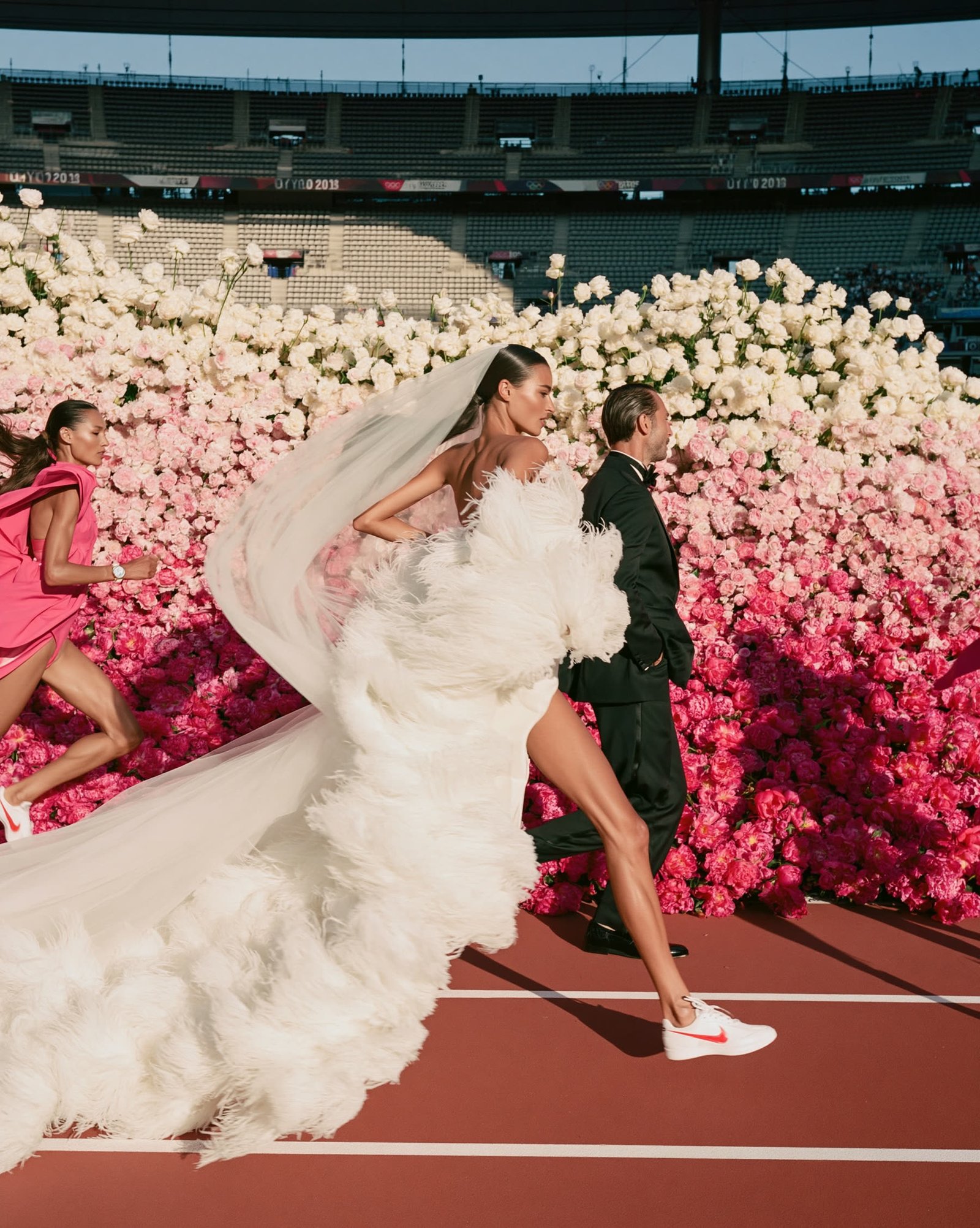 A bride and a partner in black racing across a rose-petal stadium track