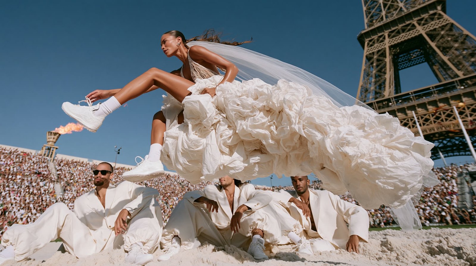 Bride mid long-jump in front of the Eiffel Tower as grooms lie below and the Olympic flame burns