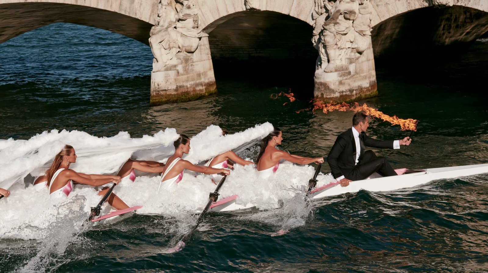 A team of brides rowing a boat down the Seine beneath a historic Paris bridge